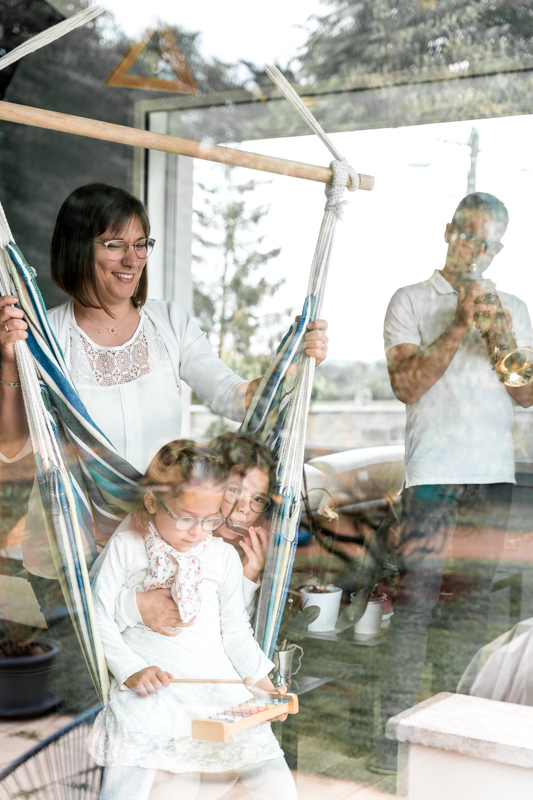 Amelie Charlet photographe séance photo famille qui joue d'un instrument de famille à travers un reflet de vitre