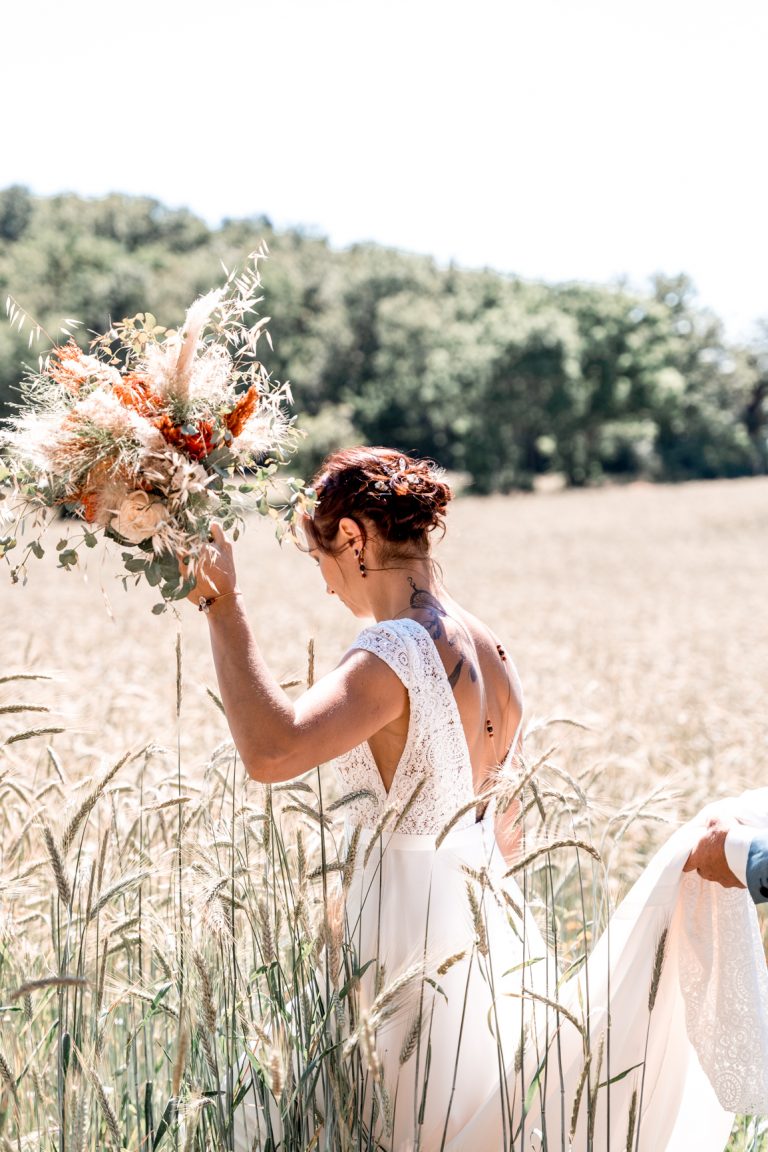 mariée dans un champs d'herbes folles avec son bouquet à la main